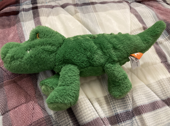 Grünes, flauschiges Gator-Plüschtier auf einem Bett