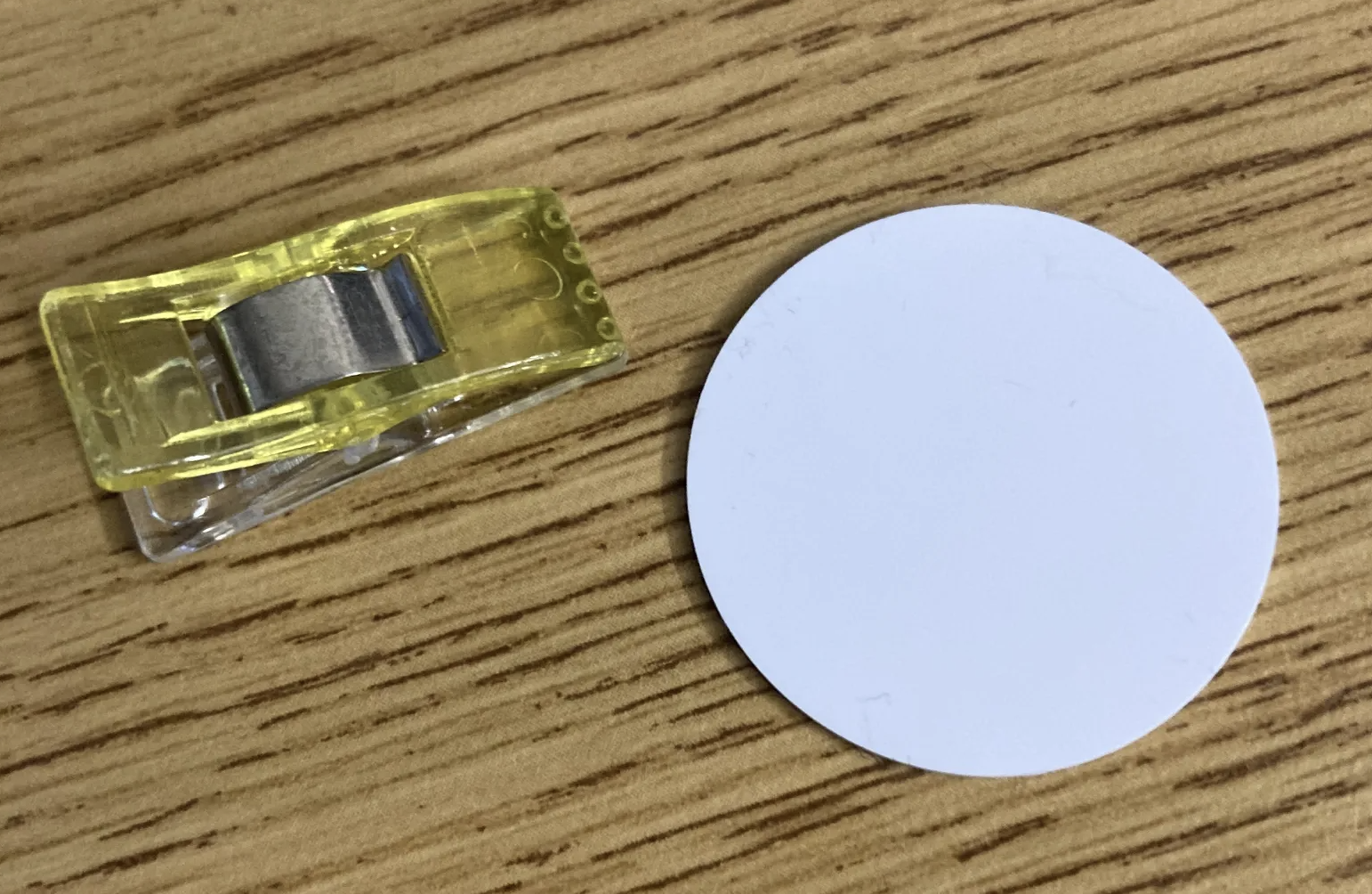 Ein weißer runder NFC-Tag neben einer Nähklammer zum Größenvergleich