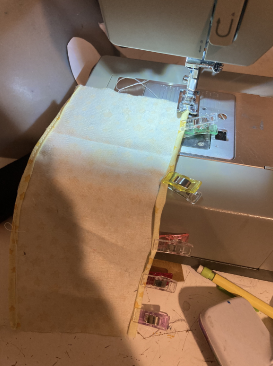 Eine Kante des bedruckten Baumwollstoffs wird mit einer Nähmaschine genäht. Eine weitere Seite ist bereits genäht.